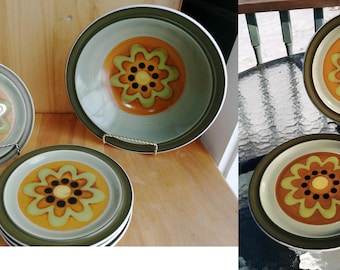 May include: A set of vintage ceramic plates and a bowl. The plates and bowl have a floral pattern with a yellow centre, surrounded by orange, green, and brown details, and a green border.