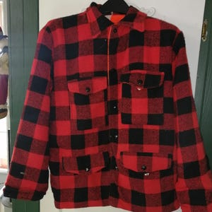 Puede incluir: Una camisa de franela a cuadros rojos y negros con cierre de botones y dos bolsillos grandes. La camisa está hecha de un material grueso y cálido.