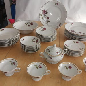 Puede incluir: Juego de vajilla antiguo de porcelana blanca con diseño de rosas. El juego incluye platos, cuencos, platillos, tazas y azucarero. Cada pieza tiene un borde dorado y un patrón de rosas burdeos.