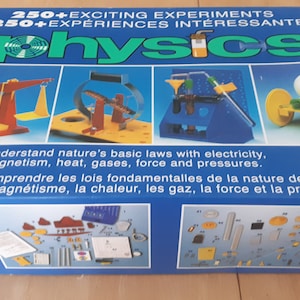 Könnte beinhalten: Eine blaue Box mit den Worten "250+ EXCITING EXPERIMENTS" und "250+ EXPÉRIENCES INTÉRESSANTES" auf der Oberseite. Die Box zeigt ein Bild einer Waage, eines Flaschenzugs, einer Wasserpumpe und eines Autos auf der Vorderseite. Die Box hat auch das Wort "Physics" in großen Buchstaben auf der Vorderseite. Die Box ist mit "12+" gekennzeichnet.