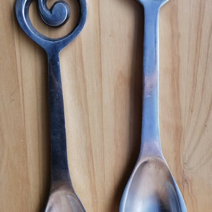 May include: A set of two silver salad serving utensils with a treble clef design. The utensils are made of metal and have a polished finish.