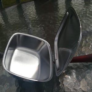 Op de afbeelding: Een roestvrijstalen, vierkante voedselwarmer met een scharnierend deksel. Het deksel is open en onthult de binnenkant. De handgreep is van donker hout. De warmer staat op een glazen tafel.