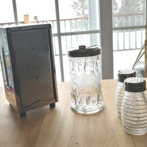 May include: Three glass containers with silver lids. The containers are clear and have a textured design. The containers are on a wooden surface.