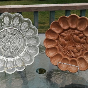 May include: Two vintage egg plates, one clear glass and one brown ceramic with a floral design. Both plates have 12 individual indentations for eggs.