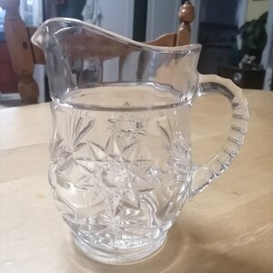 Peut inclure: Un pichet en verre transparent avec un motif en forme d'étoile. Le pichet a une poignée et une large ouverture.