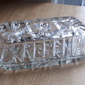 Peut inclure: Un beurrier en verre transparent avec un couvercle. Le plat est décoré d'un motif de étoiles et de lignes. Le couvercle a un motif similaire.