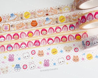 May include: A collection of decorative washi tape rolls featuring various cute character designs. The tapes showcase repeating patterns of animals, food items, and other whimsical illustrations in pastel colors. The brand name "breadycheeks" is visible on some rolls.