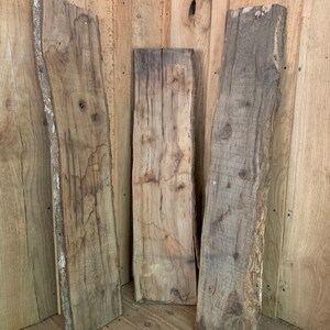 May include: Three pieces of rough-cut wood with a natural, rustic finish. The wood is light brown with a grain pattern. The wood is stacked on top of each other.