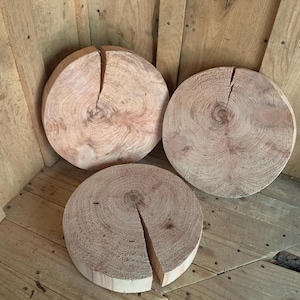May include: Three round wooden coasters with a natural wood grain. Each coaster has a crack or split, adding a rustic touch. The coasters are arranged on a wooden surface, showcasing their natural color and texture.
