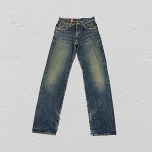May include: Blue denim jeans with a faded wash. The jeans have a classic five-pocket design, a button and zipper closure, and a straight leg. The denim has a worn appearance, with lighter areas on the thighs and knees.