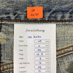 May include: Close-up of blue denim jeans with a tag that reads "JN 3290." The tag also includes measurements: waist 29 inches, front rise 11 inches, hips 44 inches, thigh 12.5 inches, knee 9 inches, leg opening 16 inches, inseam 29 inches, and outseam 41 inches.