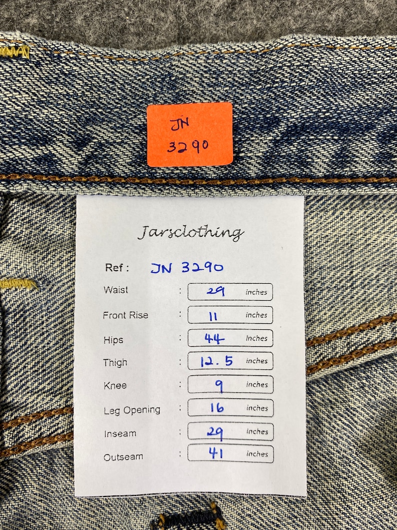 May include: Close-up of blue denim jeans with a tag that reads "JN 3290." The tag also includes measurements: waist 29 inches, front rise 11 inches, hips 44 inches, thigh 12.5 inches, knee 9 inches, leg opening 16 inches, inseam 29 inches, and outseam 41 inches.