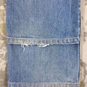 K&ouml;nnte beinhalten: Nahaufnahme einer hellblauen Jeans. Der Saum der Jeans ist ausgefranst und abgenutzt, mit sichtbaren F&auml;den. Der Stoff hat eine klassische Denim-Textur und -Farbe.
