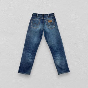 May include: A pair of blue denim jeans with a brown leather patch on the back pocket that says "Wrangler".