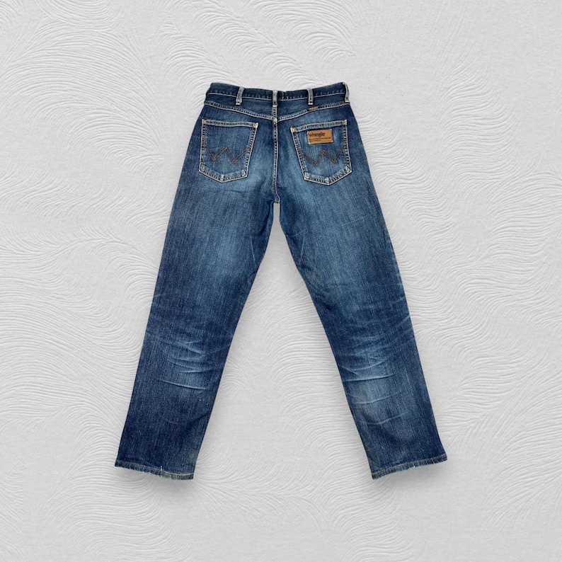 May include: A pair of blue denim jeans with a brown leather patch on the back pocket that says "Wrangler".