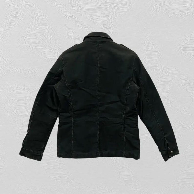 May include: A dark green jacket with a button-down front, collar, and long sleeves. The jacket has a tailored fit and appears to be made of a durable fabric. The back view shows the jacket's seams and construction details.