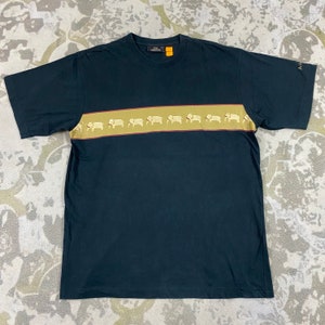 Pode incluir: Camiseta preta de manga curta com uma faixa horizontal bege no peito. A faixa apresenta um padr&atilde;o repetido de ilustra&ccedil;&otilde;es de elefantes brancos. A camiseta tem gola redonda e a marca "J.M. Thompson" &eacute; vis&iacute;vel.