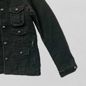 May include: Dark green jacket with multiple front pockets and decorative silver buttons. The jacket features a zipper closure and a buttoned cuff on the sleeve. The fabric appears to be a durable, possibly military-inspired material.