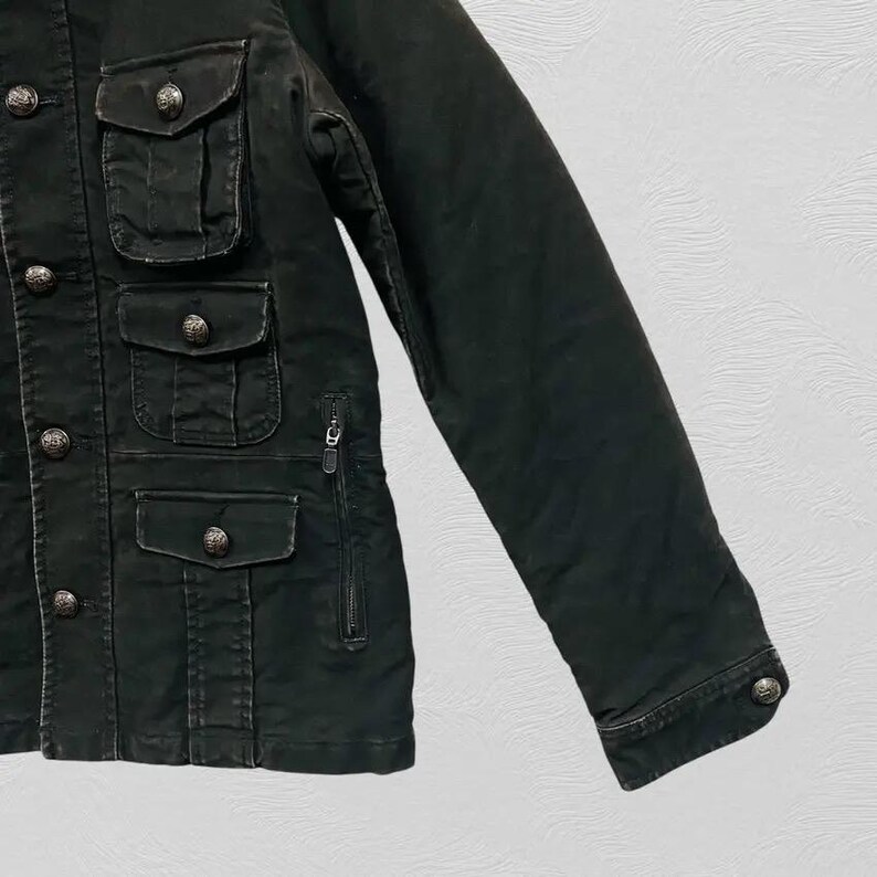 May include: Dark green jacket with multiple front pockets and decorative silver buttons. The jacket features a zipper closure and a buttoned cuff on the sleeve. The fabric appears to be a durable, possibly military-inspired material.