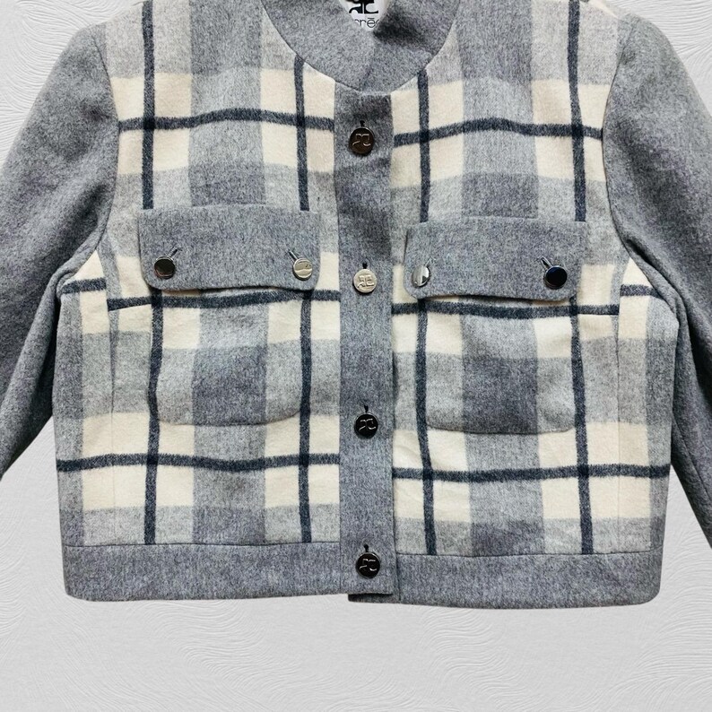 K&ouml;nnte beinhalten: Grau-wei&szlig; karierte Jacke mit rundem Ausschnitt und langen &Auml;rmeln. Die Jacke hat zwei Vordertaschen und dekorative Kn&ouml;pfe vorne. Das Karomuster ist eine Mischung aus grauen, wei&szlig;en und schwarzen Linien.