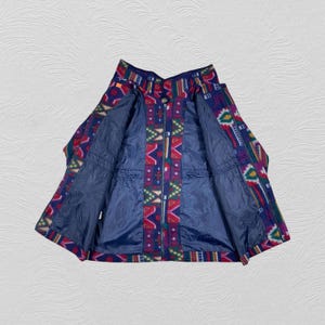 May include: A colorful fleece jacket with a geometric pattern in red, blue, green, and yellow. The jacket has a full zipper and a blue interior lining. The open jacket displays the interior pockets.