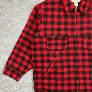 Op de afbeelding: Rood-zwarte geruite jas met een volledige ritssluiting. De jas heeft twee voorzakken en een kleine borstzak. Gemaakt van een dik, warm materiaal, perfect voor koud weer. Het patroon is een klassieke buffelruit.