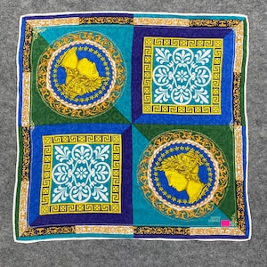 Peut inclure: Foulard carré en soie avec un motif géométrique dans les tons de bleu, vert et or. Le foulard présente quatre quadrants avec des motifs ornés et un médaillon central avec un portrait de profil. Les bords sont bordés d'une bordure blanche.