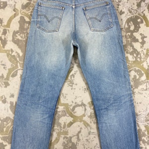 K&ouml;nnte beinhalten: Hellblaue Jeans mit klassischem F&uuml;nf-Taschen-Design. Die Jeans haben eine verwaschene Optik und einen geraden Beinverlauf. Die Ges&auml;&szlig;taschen haben eine markante geschwungene Naht. Die Jeans liegen flach auf einer gemusterten Oberfl&auml;che.