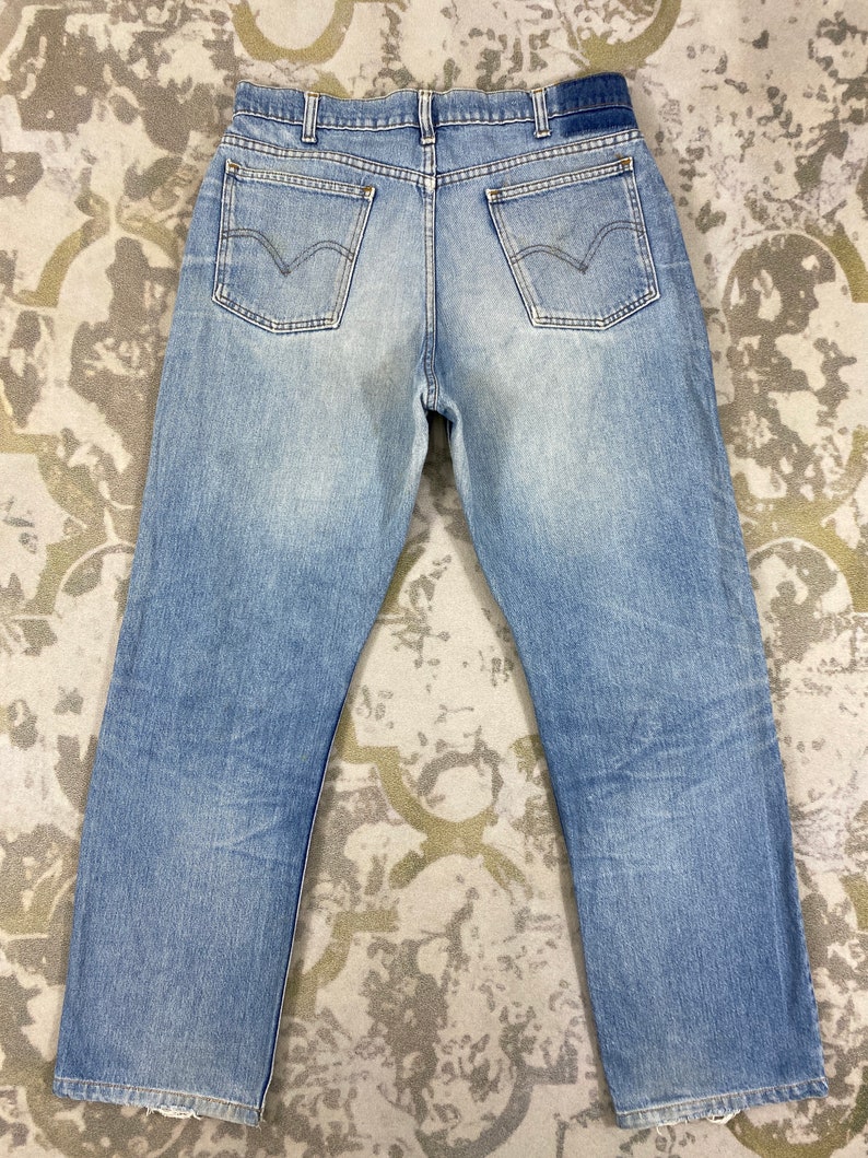 K&ouml;nnte beinhalten: Hellblaue Jeans mit klassischem F&uuml;nf-Taschen-Design. Die Jeans haben eine verwaschene Optik und einen geraden Beinverlauf. Die Ges&auml;&szlig;taschen haben eine markante geschwungene Naht. Die Jeans liegen flach auf einer gemusterten Oberfl&auml;che.