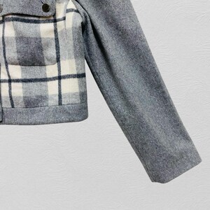 K&ouml;nnte beinhalten: Graue Wolljacke mit einem Karomuster in Wei&szlig;, Grau und Schwarz. Die Jacke hat einen Knopfverschluss und eine einzelne Tasche. Der &Auml;rmel ist einfarbig grau.
