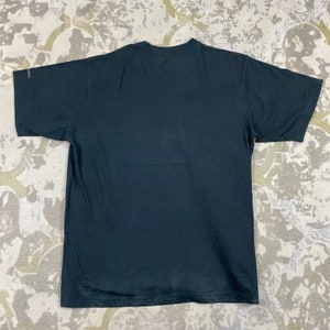 Pode incluir: Uma camiseta preta com gola redonda e mangas curtas. A camisa &eacute; feita de um material macio e tem um design simples e cl&aacute;ssico. A camisa est&aacute; estendida em uma superf&iacute;cie estampada.