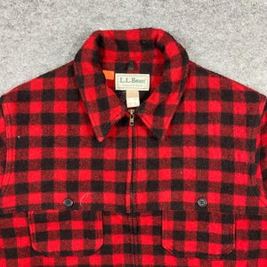 Op de afbeelding: Rood en zwart geruit jack met ritssluiting, twee voorzakken en een kraag. De jas heeft het L.L.Bean-label op de kraag. De jas is gemaakt van een dik, warm materiaal.