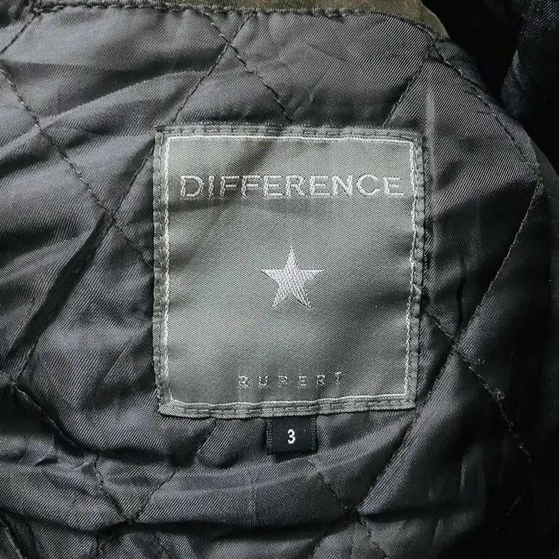 May include: Close-up of a quilted jacket lining. A rectangular label with the word "DIFFERENCE" is stitched on the lining. Below the word is a star and the name "RUPERT". The number "3" is below the name.