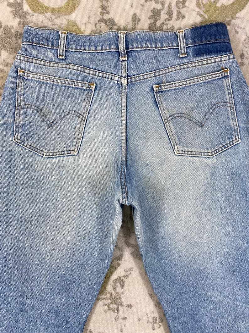 K&ouml;nnte beinhalten: Hellblaue Jeans mit zwei Ges&auml;&szlig;taschen und dem Levi's-Logo. Die Jeans haben eine verwaschene Optik und ein klassisches F&uuml;nf-Taschen-Design. Die R&uuml;ckseite der Jeans ist sichtbar und zeigt Bund und G&uuml;rtelschlaufen.