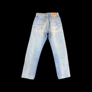 May include: Light blue denim jeans featuring a high-rise waist, two back pockets with arcuate stitching, a tan leather-like patch on the waistband, and a small red tab on the right back pocket. The denim has a faded wash with straight legs.