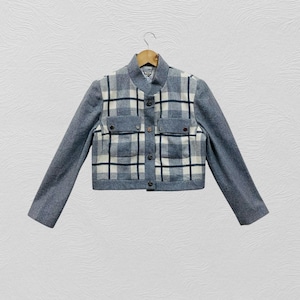 K&ouml;nnte beinhalten: Eine kurze Jacke mit grauem K&ouml;rper und &Auml;rmeln. Die Vorderseite hat ein Karomuster in Wei&szlig;, Marineblau und Grau, mit zwei kleinen Taschen und schwarzen Kn&ouml;pfen. Die Jacke h&auml;ngt an einem Holzb&uuml;gel.