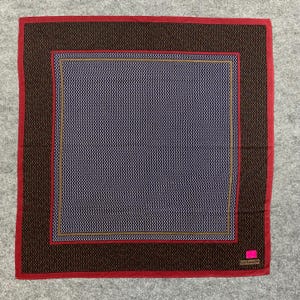 Peut inclure: Un foulard carré avec une bordure marron foncé et un bord rouge. Le centre présente un motif géométrique bleu marine et blanc. Une petite étiquette rose se trouve dans le coin inférieur droit.