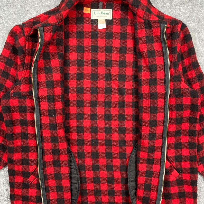 Op de afbeelding: Rood en zwart geruite jas met ritssluiting en het label L.L.Bean. De jas is open en toont de binnenvoering en een lange ritssluiting. Het patroon is een klassiek, vet geruit ontwerp.