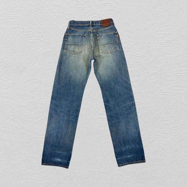 May include: Faded blue denim jeans with a classic five-pocket design. The jeans have a straight leg cut and a worn appearance, with a brown leather patch on the back waistband. The jeans are a size 32x32.
