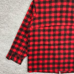 Op de afbeelding: Rood en zwart geruit jack. De jas heeft een klassiek buffelruitpatroon. De mouw heeft een manchet met knoop. De jas is gemaakt van een dik, warm materiaal.