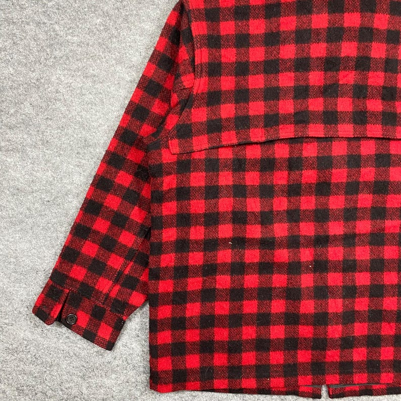 Op de afbeelding: Rood en zwart geruit jack. De jas heeft een klassiek buffelruitpatroon. De mouw heeft een manchet met knoop. De jas is gemaakt van een dik, warm materiaal.