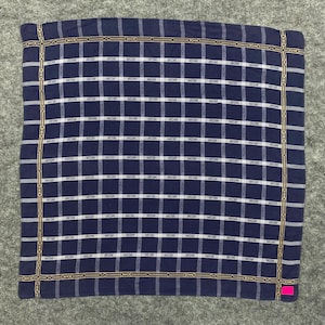 Peut inclure: Foulard carré bleu marine avec un motif quadrillé. La grille est composée de lignes blanches et des lettres "MCM" répétées dans chaque carré. La bordure présente un motif de chaîne dorée. Le foulard est en tissu doux.