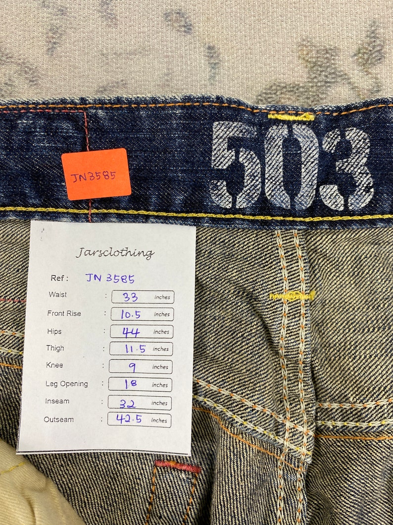 May include: Dark blue denim jeans featuring the number 503 printed in white on the waistband. A white tag displays measurements in inches: waist 33, front rise 10.5, hips 44, thigh 11.5, knee 9, leg opening 18, inseam 32, and outseam 42.5.