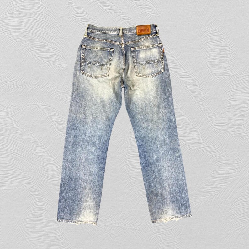 May include: Light blue denim jeans with a faded wash and a leather patch on the back. The jeans have a classic five-pocket design and a straight leg fit. The back of the jeans are visible, showing the pockets and the brand label.