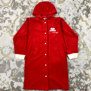 K&ouml;nnte beinhalten: Eine rote Kapuzenjacke mit wei&szlig;en B&uuml;ndchen und Knopfleiste. Auf der Brust ist das Logo "Courr&egrave;ges" in Wei&szlig; zu sehen. Die Jacke hat einen langen, geraden Schnitt und zwei Vordertaschen.