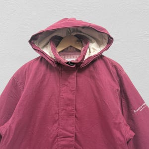 May include: A burgundy hooded jacket with a beige interior lining. The jacket has a full-length zipper and a high collar. The hood is adjustable and the jacket has a small logo on the sleeve. The jacket is made of a durable, weather-resistant material.