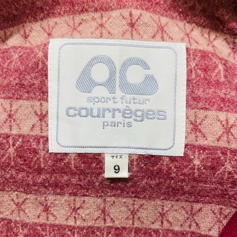 May include: Close-up of a pink and red fabric with a white label. The label features the text "AC sport futur courr&egrave;ges paris" in blue and white. The number "9" is printed below the label.