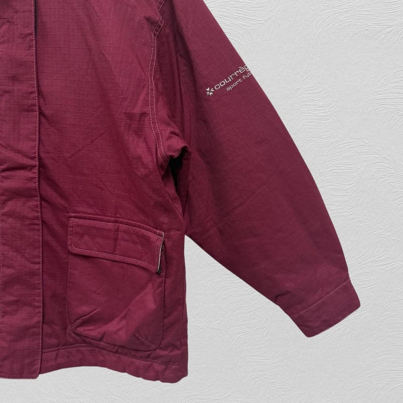 May include: A maroon jacket with a pocket and the Courr&egrave;ges logo on the sleeve. The jacket has a buttoned cuff and a flap pocket. The fabric has a textured appearance.