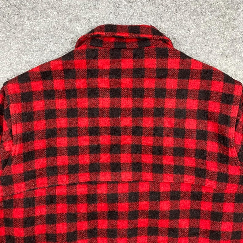 Op de afbeelding: Close-up van een rood-zwart geruit flanellen overhemd. Het overhemd heeft een klassiek buffelruitpatroon. De kraag en rugpas zijn zichtbaar, wat de constructie en stof van het kledingstuk benadrukt.