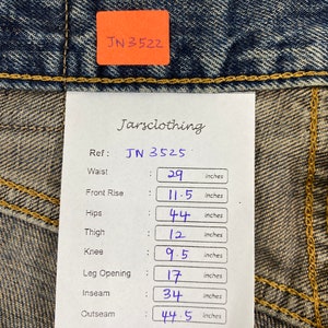 May include: Close-up of blue denim jeans with a tag displaying measurements. Waist is 29 inches, front rise 11.5 inches, hips 44 inches, thigh 12 inches, knee 9.5 inches, leg opening 17 inches, inseam 34 inches, and outseam 44.5 inches.